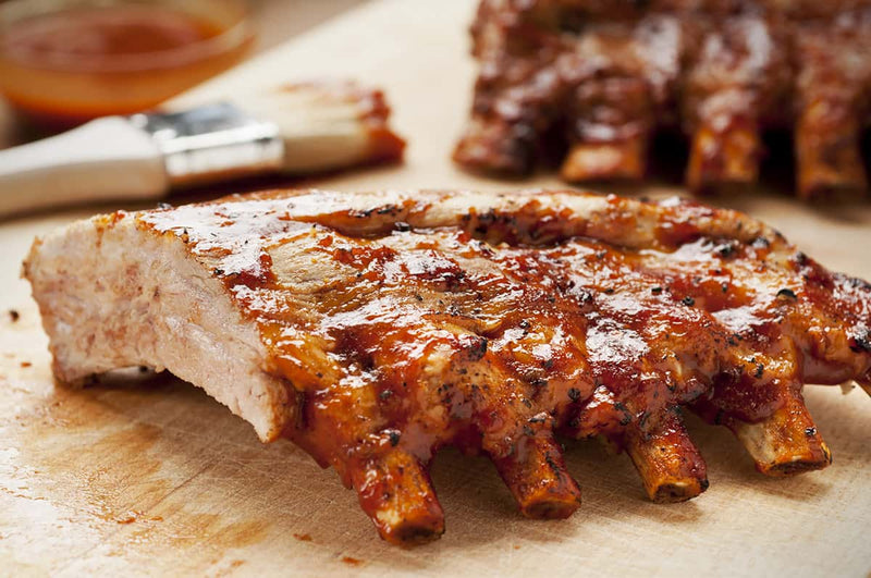 Barbecued ribs on a cutting board with a brush and sauce in the background