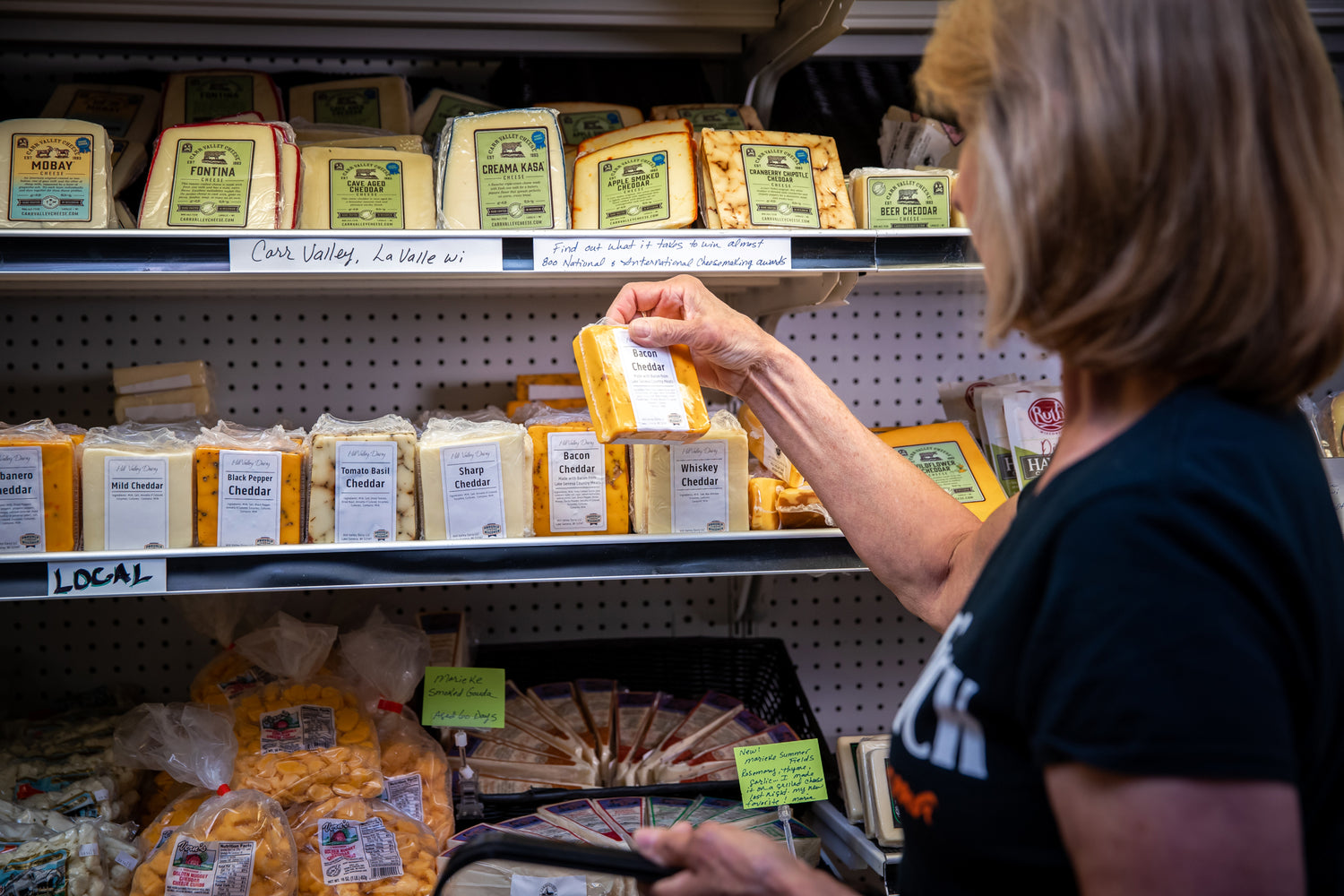 A woman taking a package of cheese off a refrigerated shelf