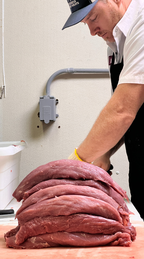 A butcher cutting a stack of pork tenderloins