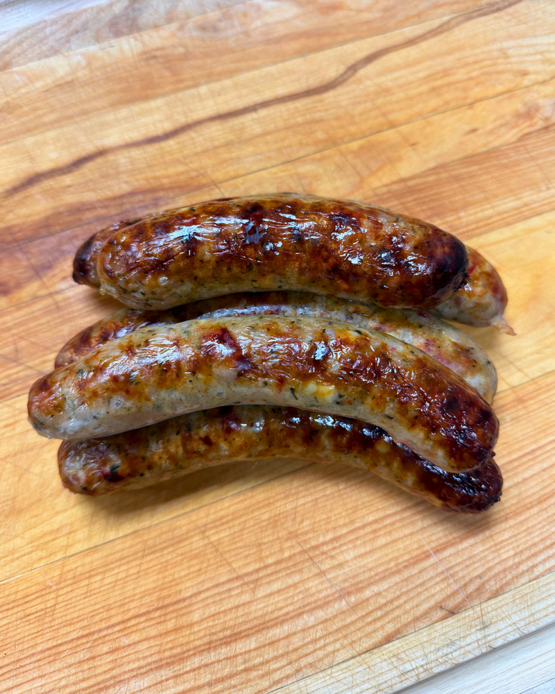 Three cooked sausages with charred grill marks resting on a wooden cutting board.