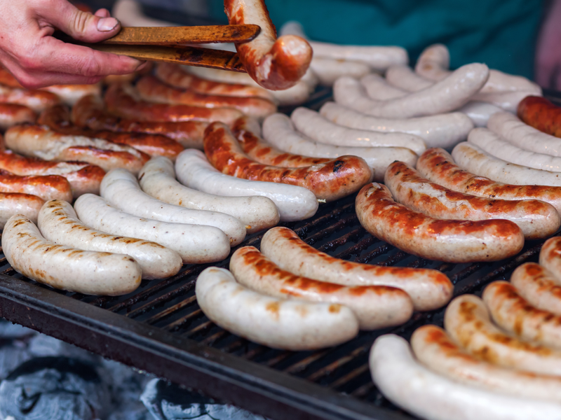Grilled sausages on a barbecue grill with a person's hand holding tongs.