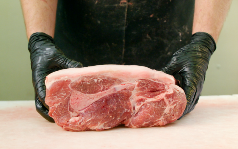 butcher holding raw bone in pork shoulder