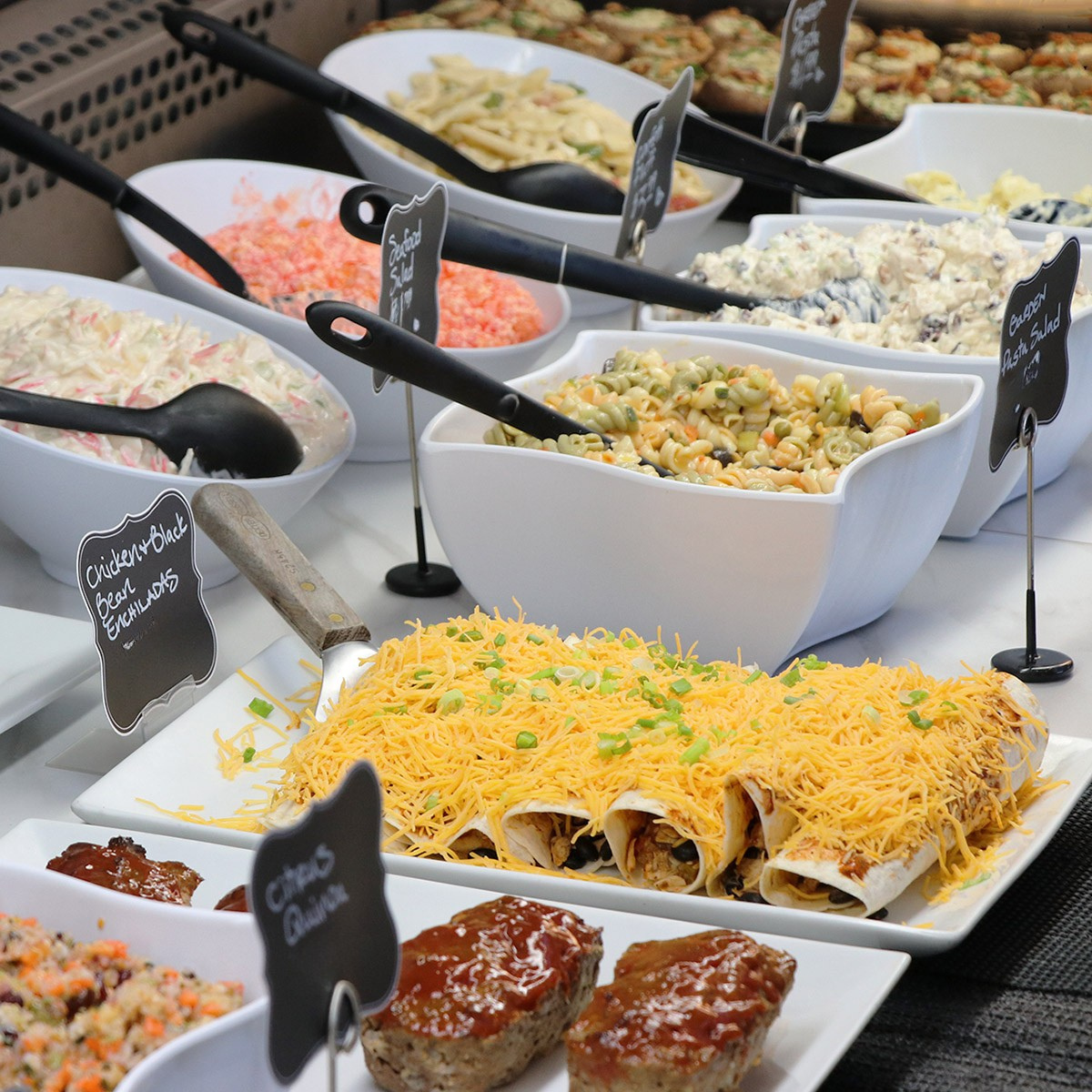 Buffet table with various food dishes including enchiladas, chicken salad, and other items.