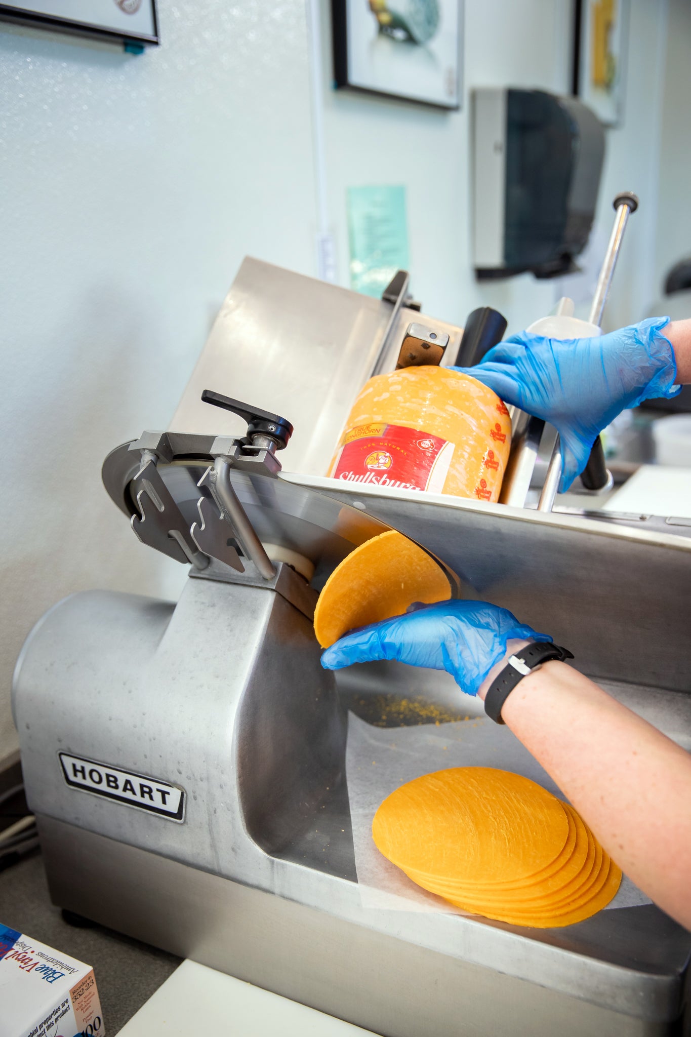 Person using a Hobart slicer to cut cheese in a kitchen setting
