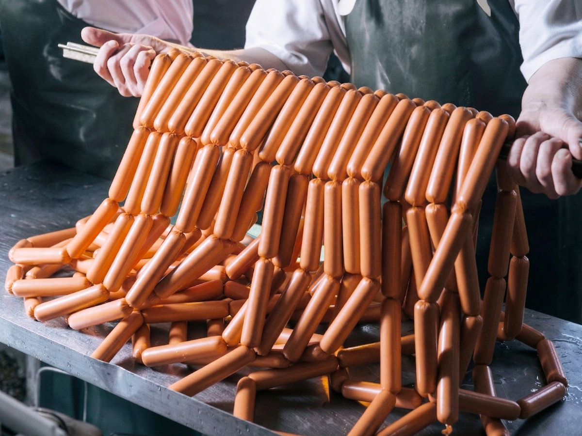 Stack of hot dogs held together by a metal frame on a dark surface.