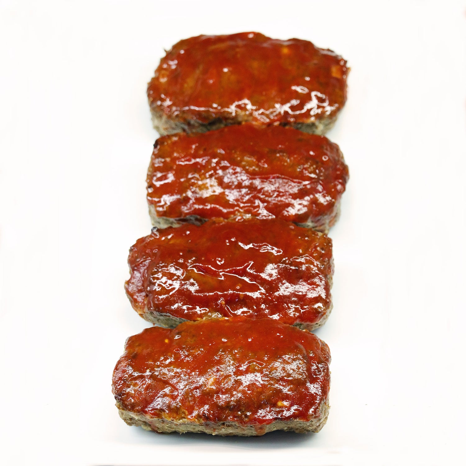 Four meatloaf slices with a glaze on a white background
