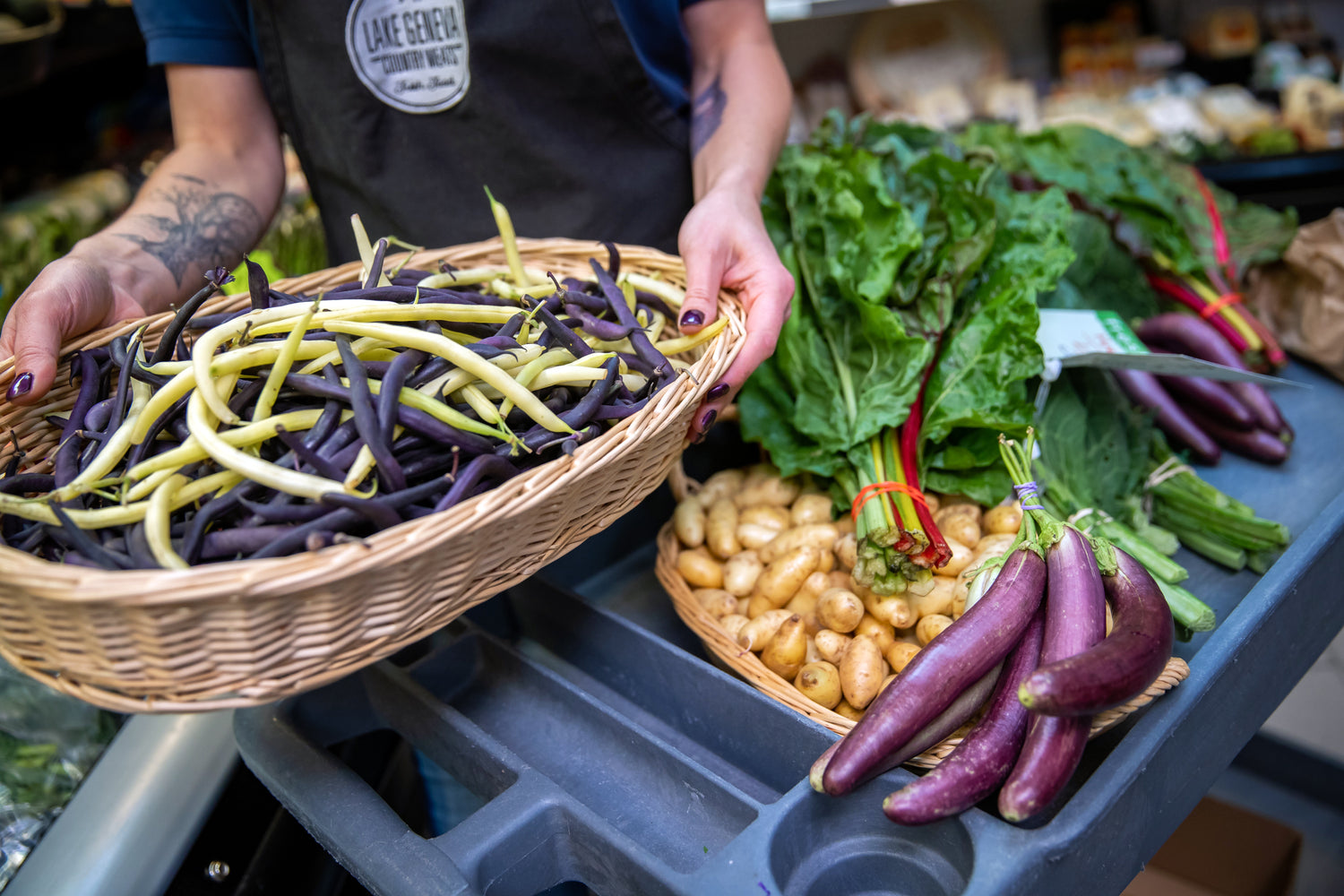 a woman holding a basket of multi color beans with other produce in view