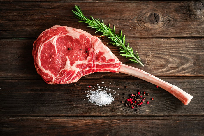 Raw tomahawk beef steak with rosemary, salt, and pepper on a wooden surface
