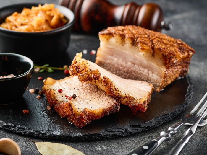 Sliced fried pork belly on a dark slate board with bowls of accompaniments.