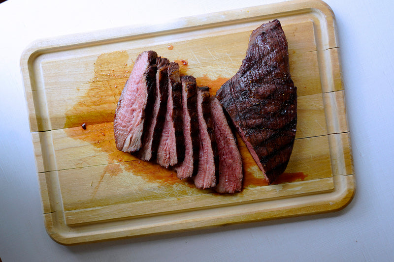 Sliced tri tip steak on a wooden cutting board with a white background