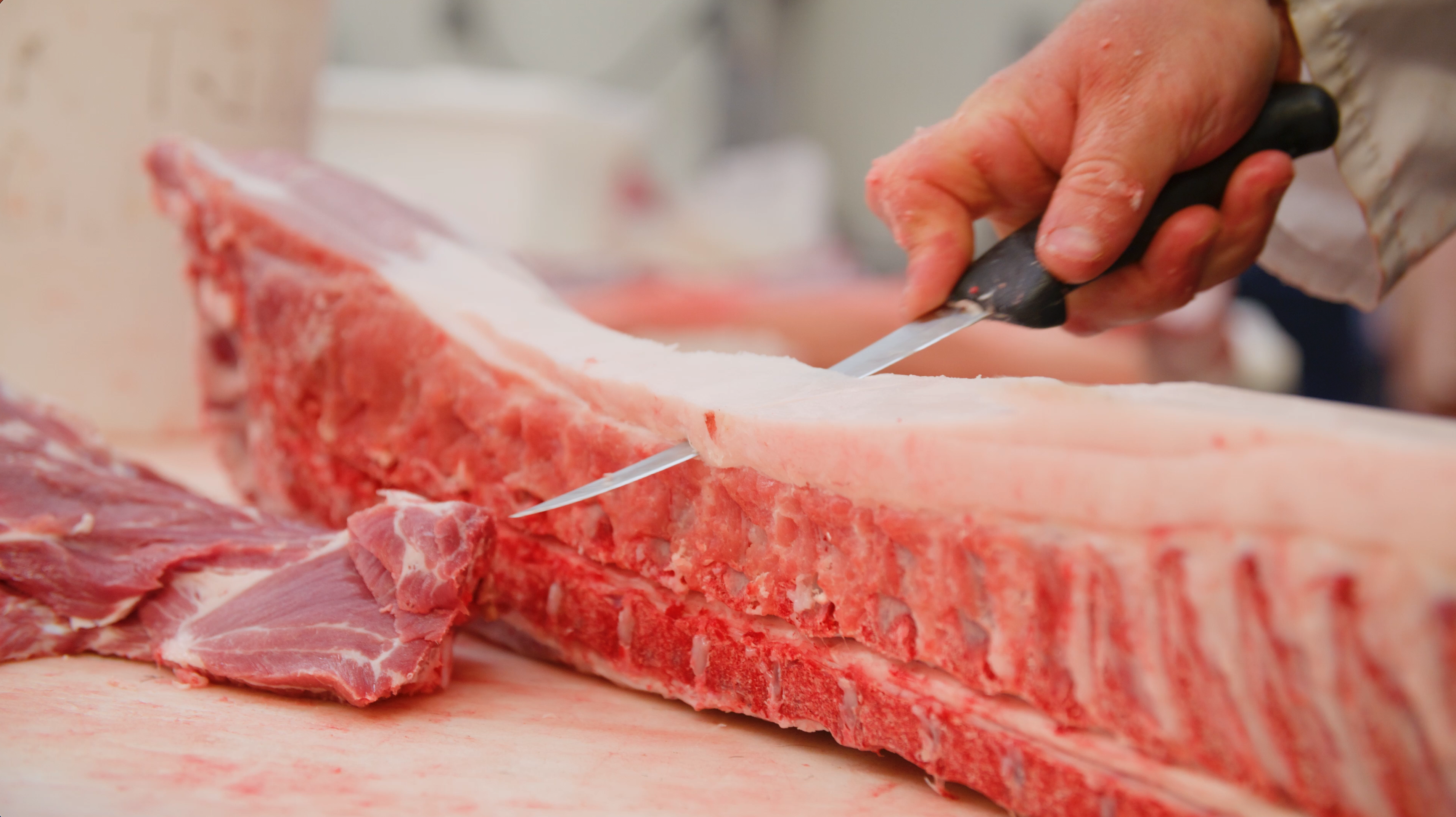 a butcher trimming fat with a knife from a bone in pork loin