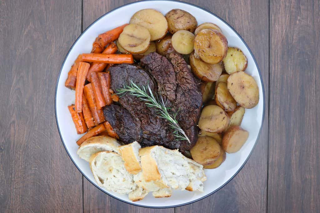 Beef roast with vegetables in a white serving tray